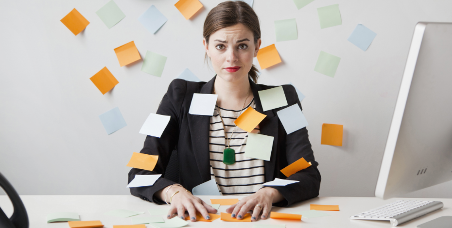A woman looks overwhelmed in the office. She is covered in post-it notes and has a frantic look on her face.