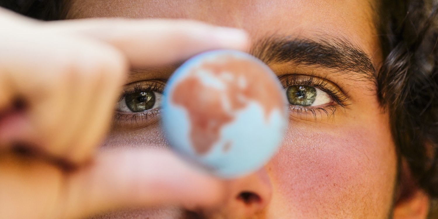 Image of a world globe being held in the fingers of a man, with his face looming large in the background.