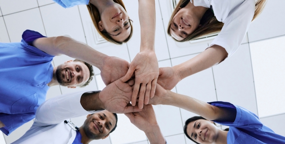 team of healthcare professionals putting right hands together in a circle and smiling photo shot from beneath them